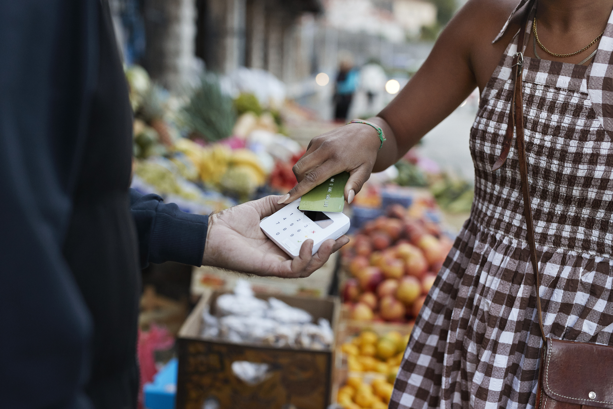 Person handing a credit card to a vendor at a produce market