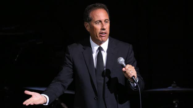 Jerry Seinfeld performs on stage in a suit, holding a microphone
