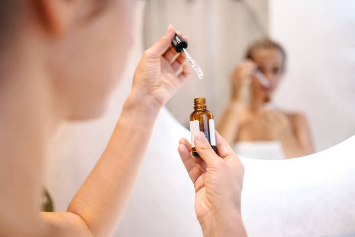 Woman applying facial serum, reflected in bathroom mirror