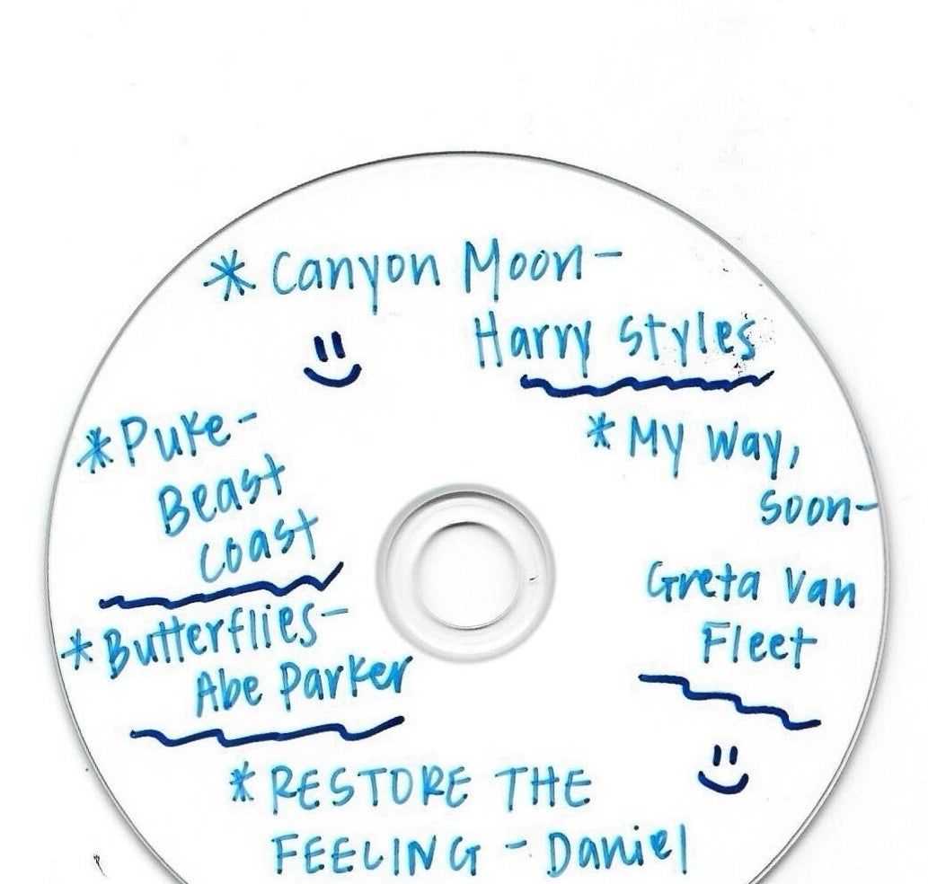 Handwritten tracklist on a white CD, including artists like Harry Styles and Daniel Caesar