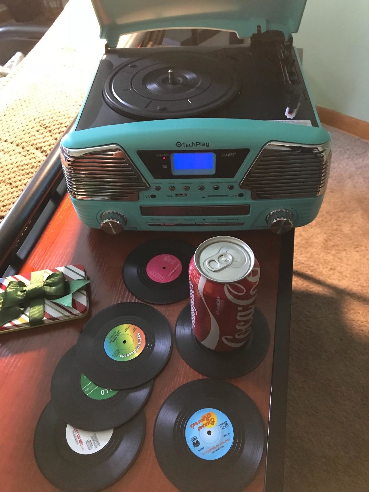 A teal turntable with small vinyl records and a Coca-Cola can on a table; a bow nearby
