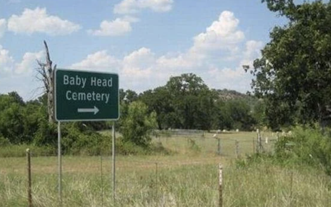 Sign pointing to &quot;Baby Head Cemetery&quot; next to a rural landscape