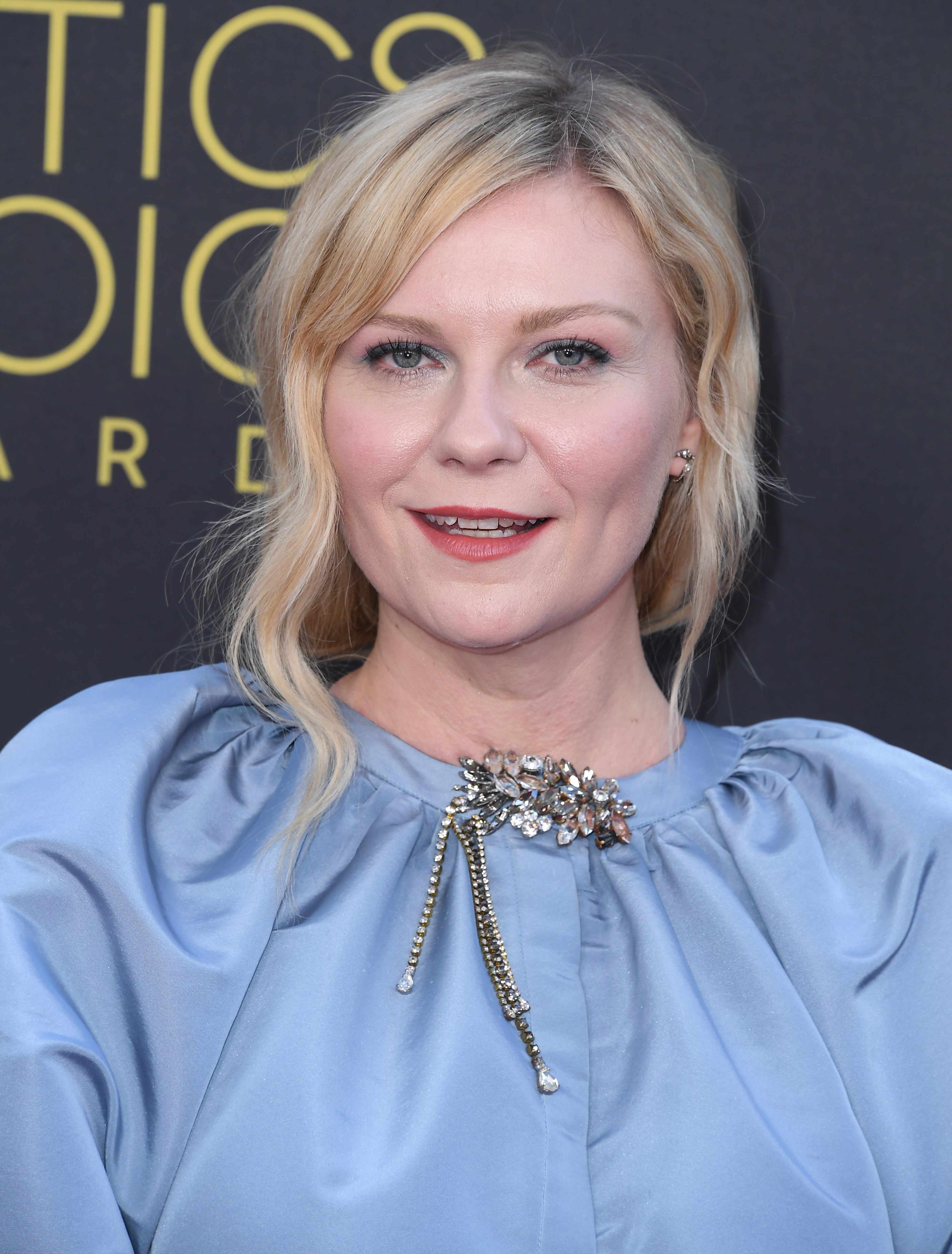 Kirsten Dunst at an event wearing a satin gown with an ornate jeweled neckline