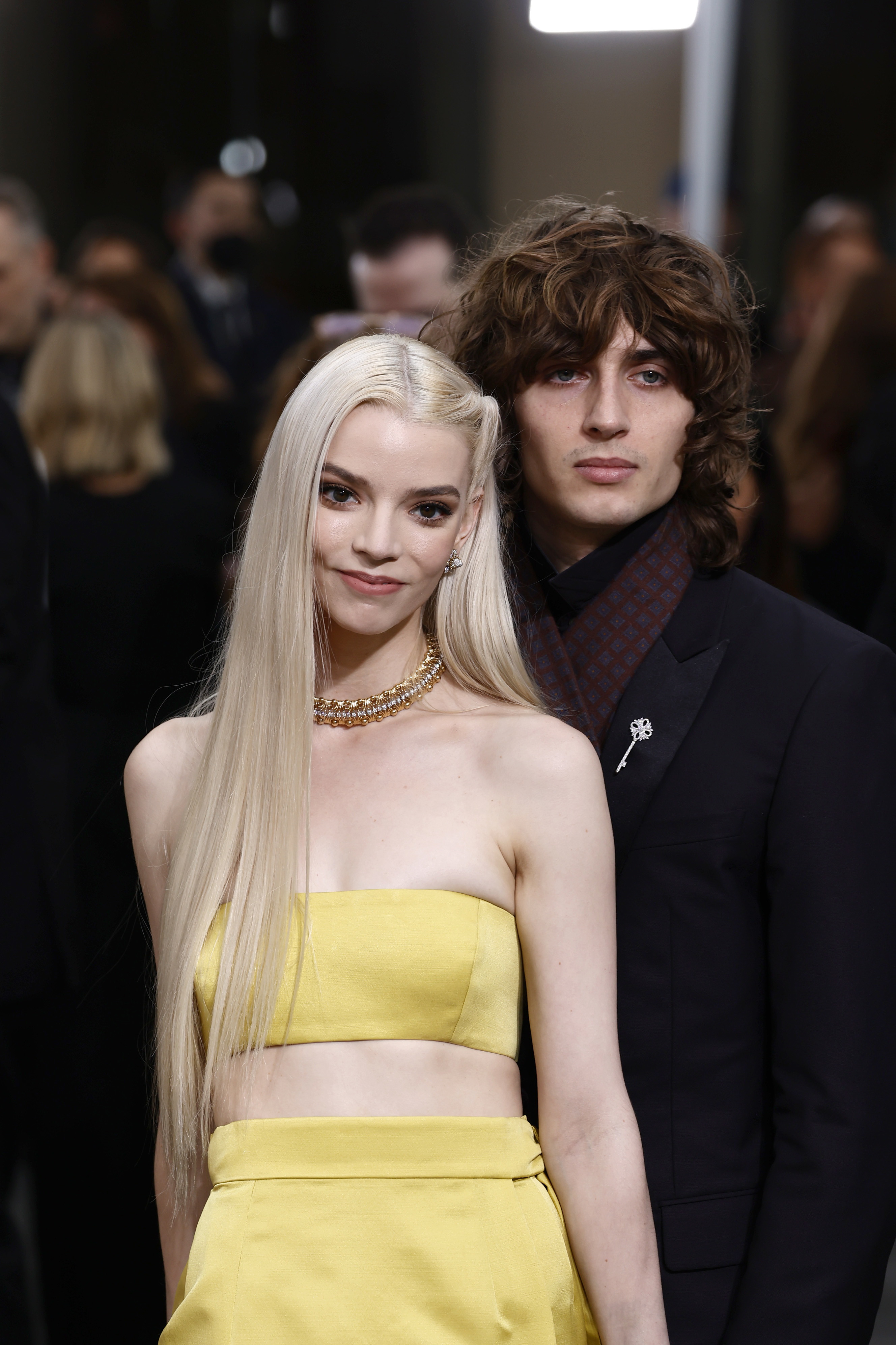 Two celebrities on red carpet; woman in strapless yellow dress with choker, man in black suit with patterned scarf