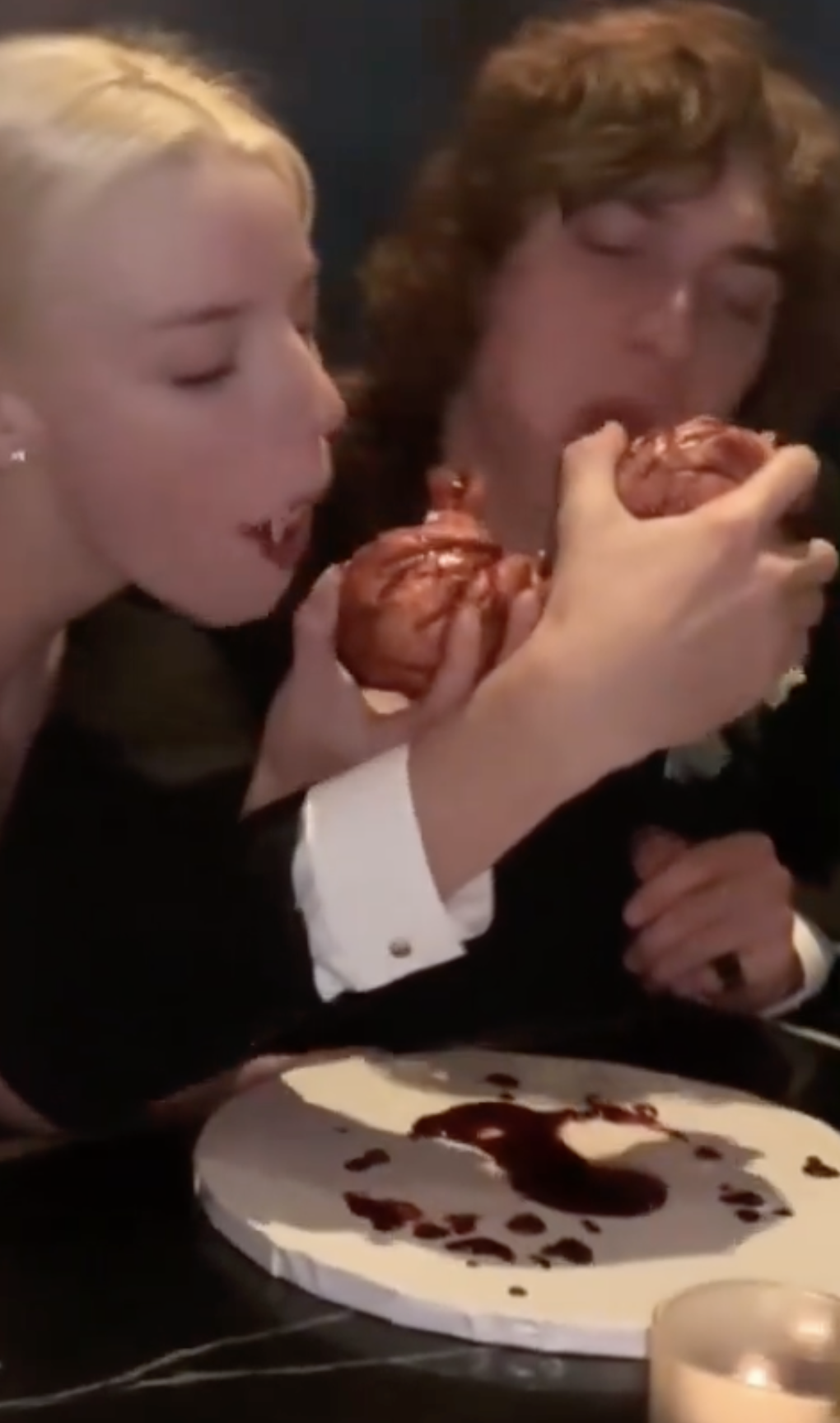 Two people eagerly biting into a shared dessert, messy with chocolate