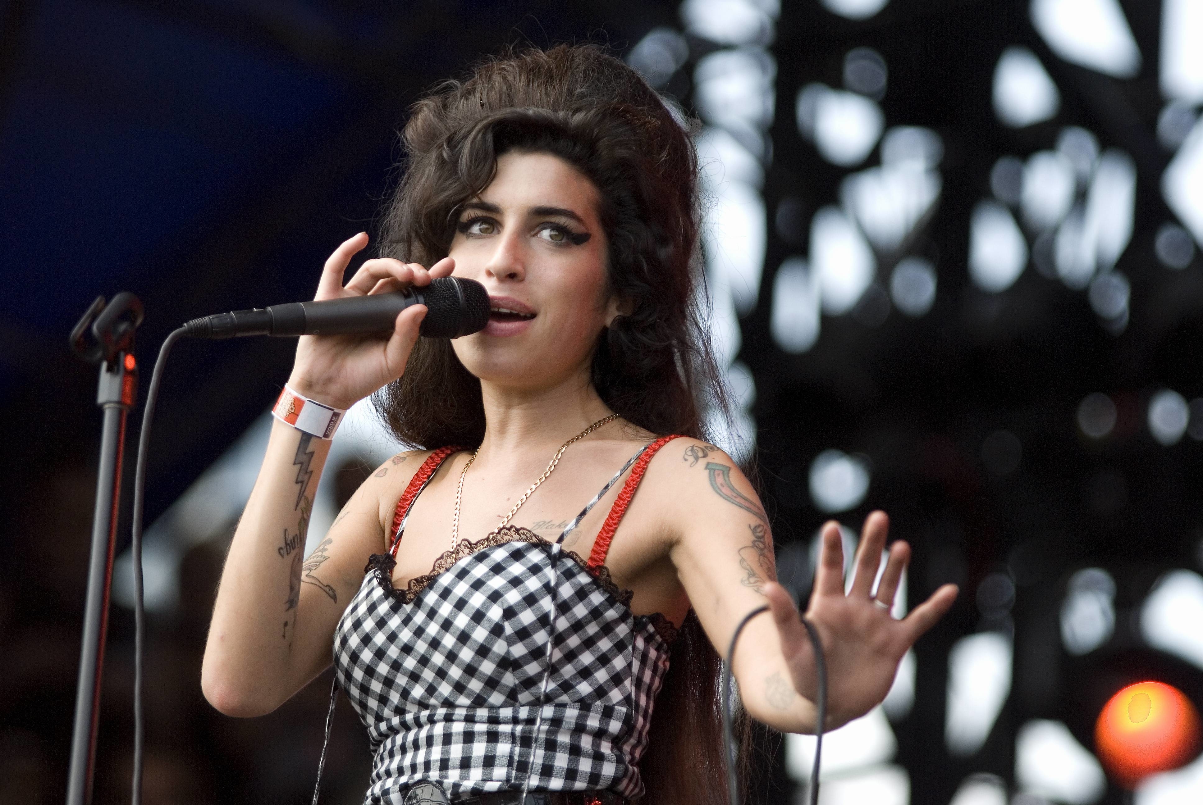 Amy Winehouse performing with a microphone, wearing a checked dress