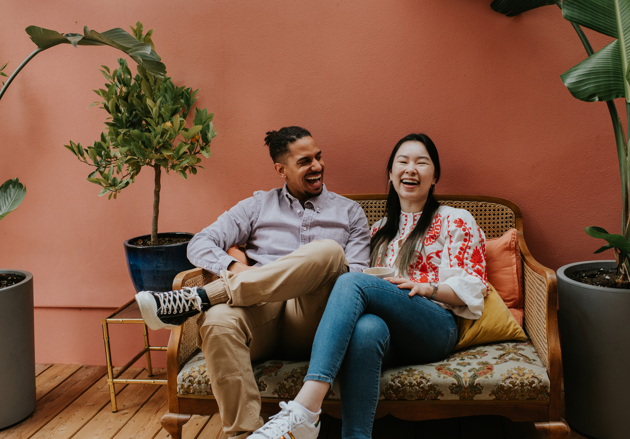 Two people sitting together on a bench, laughing, with potted plants beside them