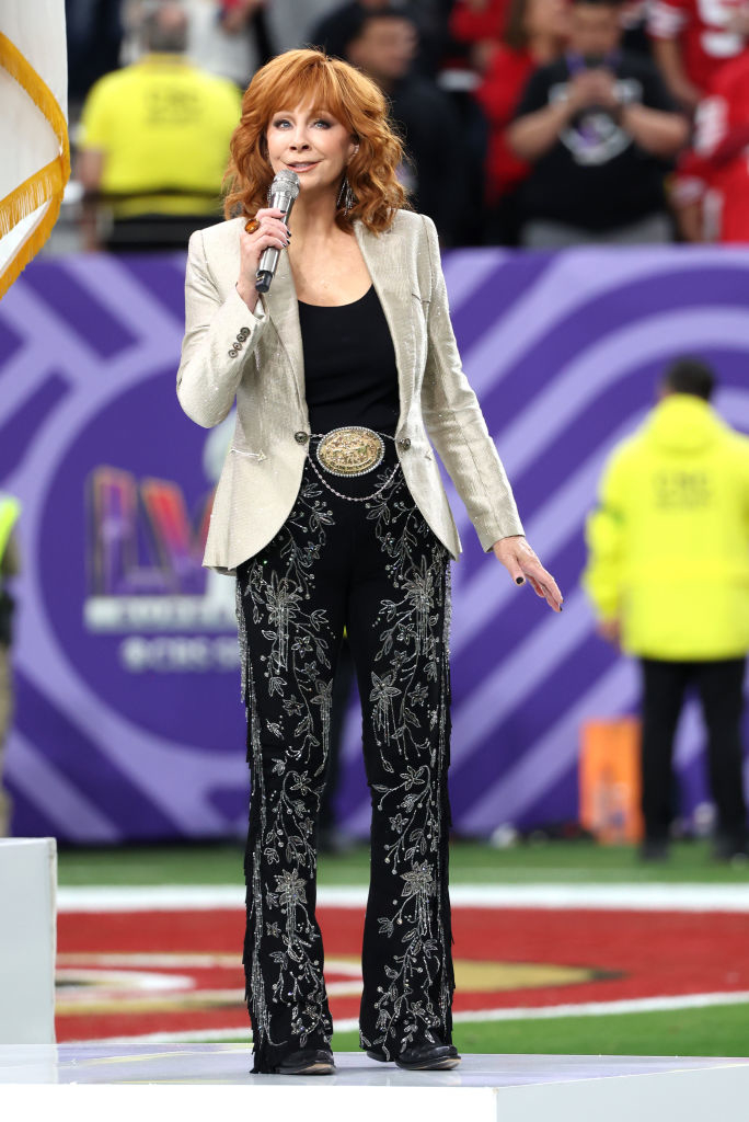 Reba McEntire wearing a shimmering blazer and patterned pants, performing at a sports event
