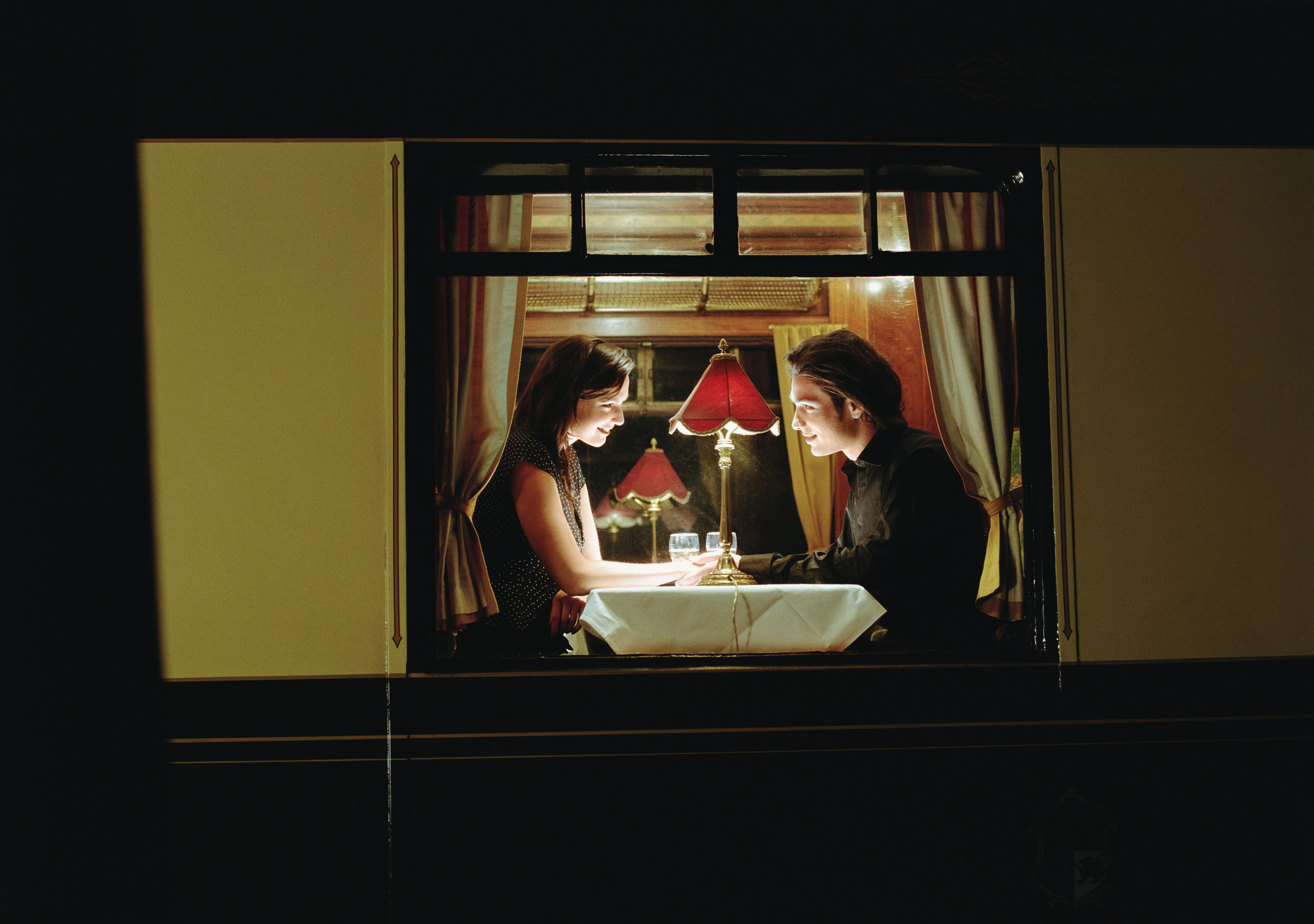 Two people having a candlelit dinner in an intimate setting, viewed through a window