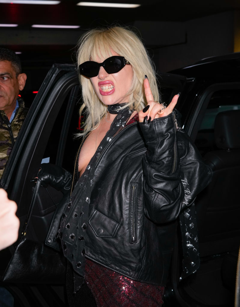 Lady Gaga in a black leather jacket and sunglasses making a rock hand gesture