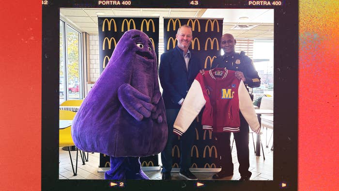 Costumed character Grimace with two men inside a McDonald&#x27;s, one holding a McDonald&#x27;s jacket, smiling