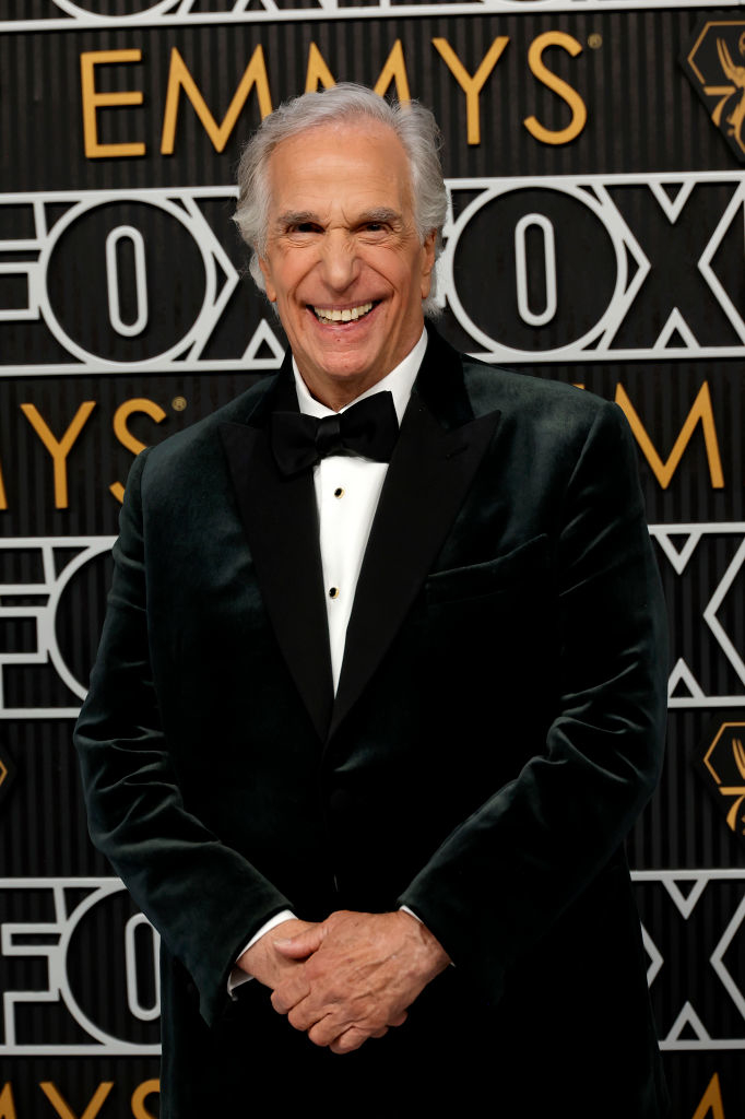Henry Winkler in black tuxedo smiling at event with patterned backdrop