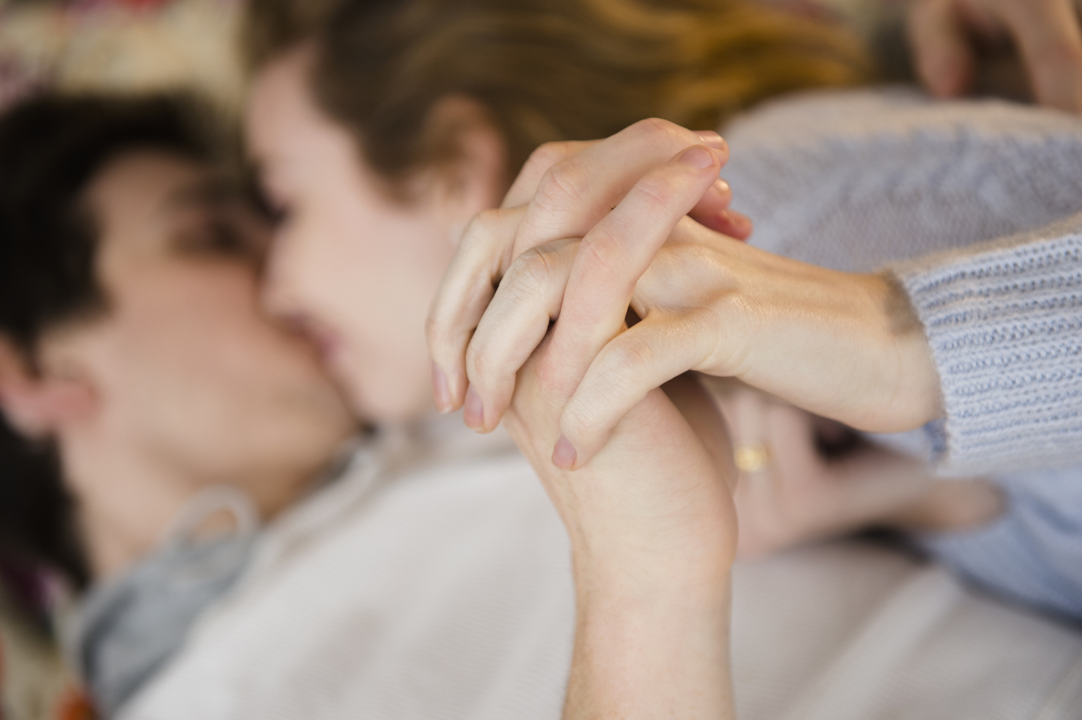 Two people in a close embrace, sharing a kiss, focus on interlocked hands