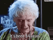 Elderly woman with necklaces speaks, subtitle reads "It's been 84 years…" from a film scene
