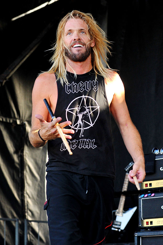 Taylor Hawkins on stage performing, wearing a casual sleeveless top and holding a microphone