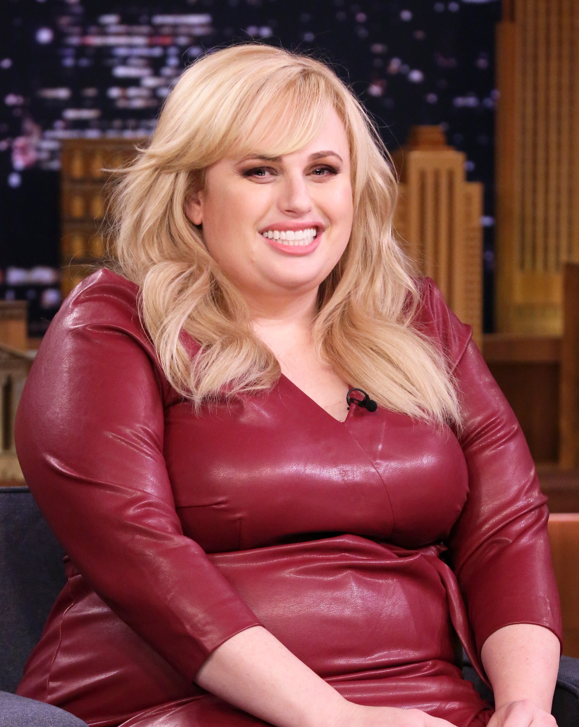 Rebel Wilson seated on a talk show set wearing a leather dress