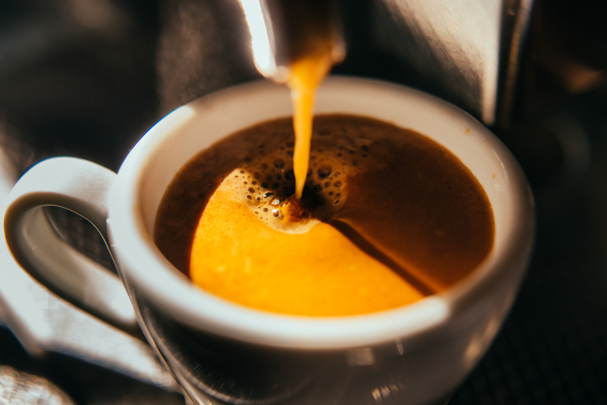 Espresso being poured into a white cup, showing the coffee's crema