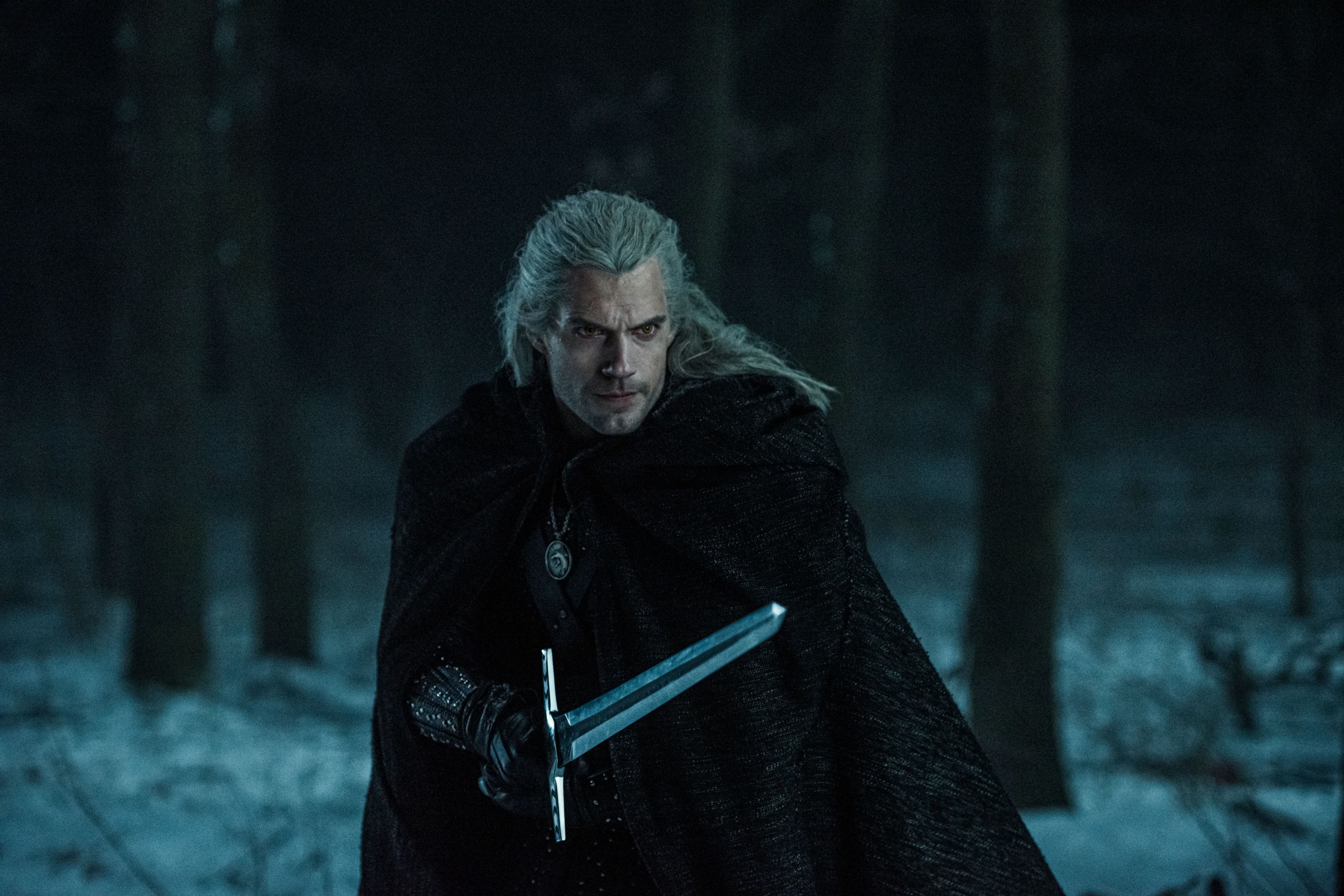 Geralt from The Witcher in a forest, with sword drawn, wearing a cloak