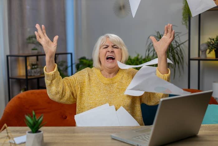 Woman looking frustrated at desk with papers flying and laptop open