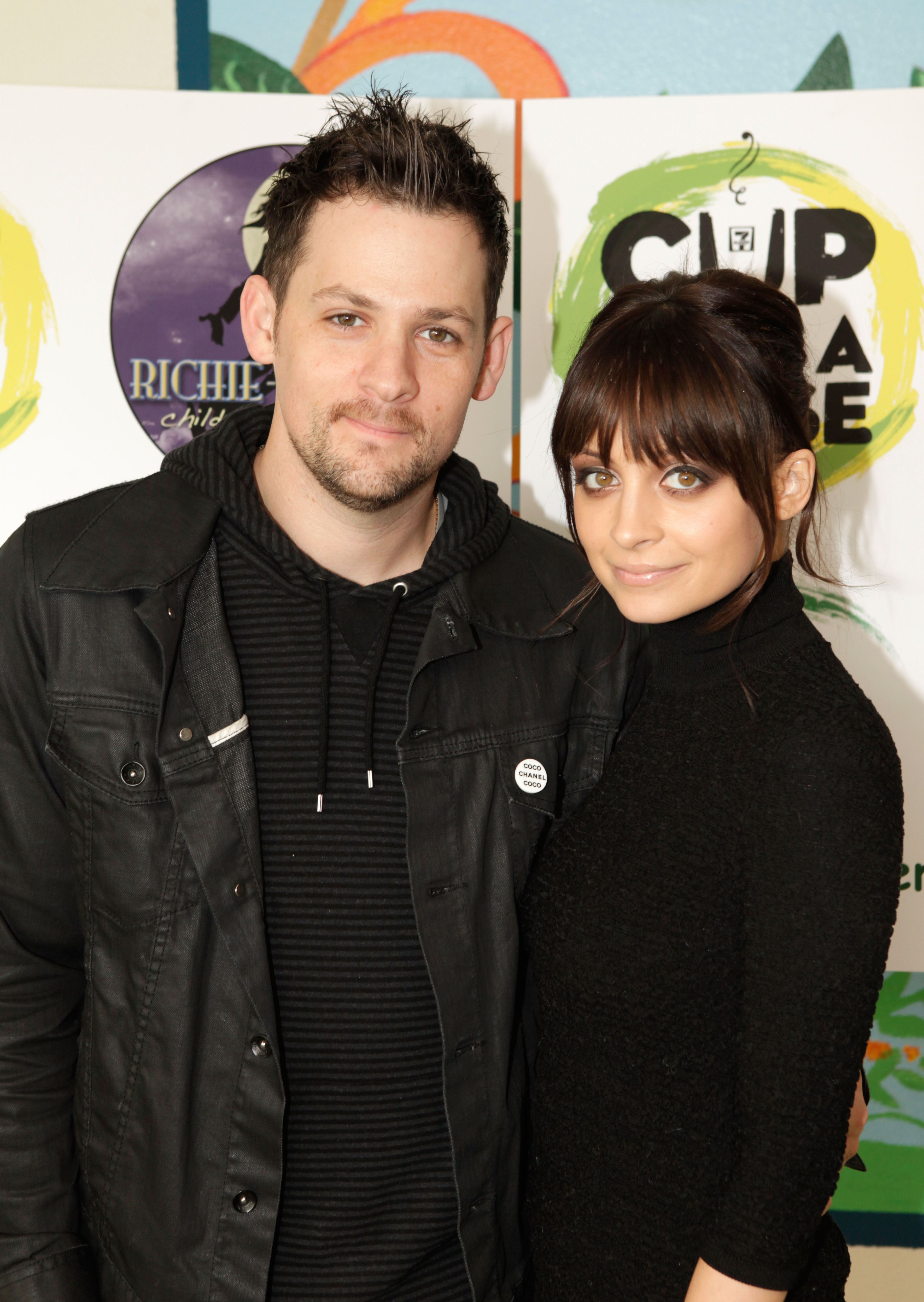 Two people posing for the camera, both dressed in dark casual attire, standing against a backdrop with logos