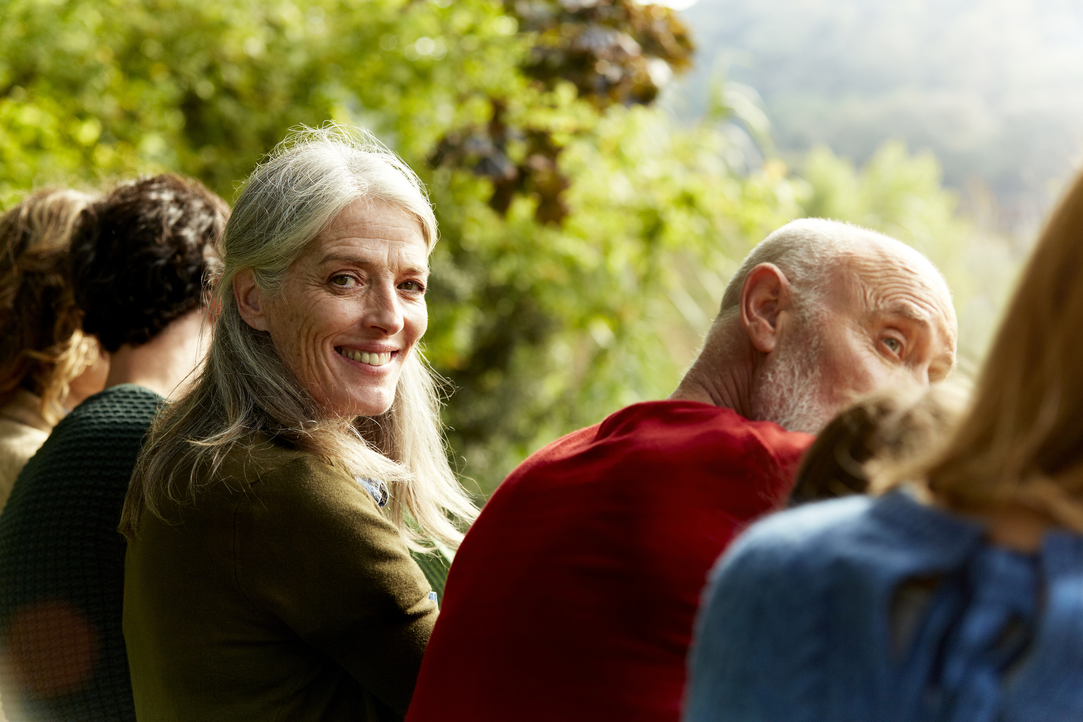 Two older adults smiling at each other with others in the foreground, outdoors