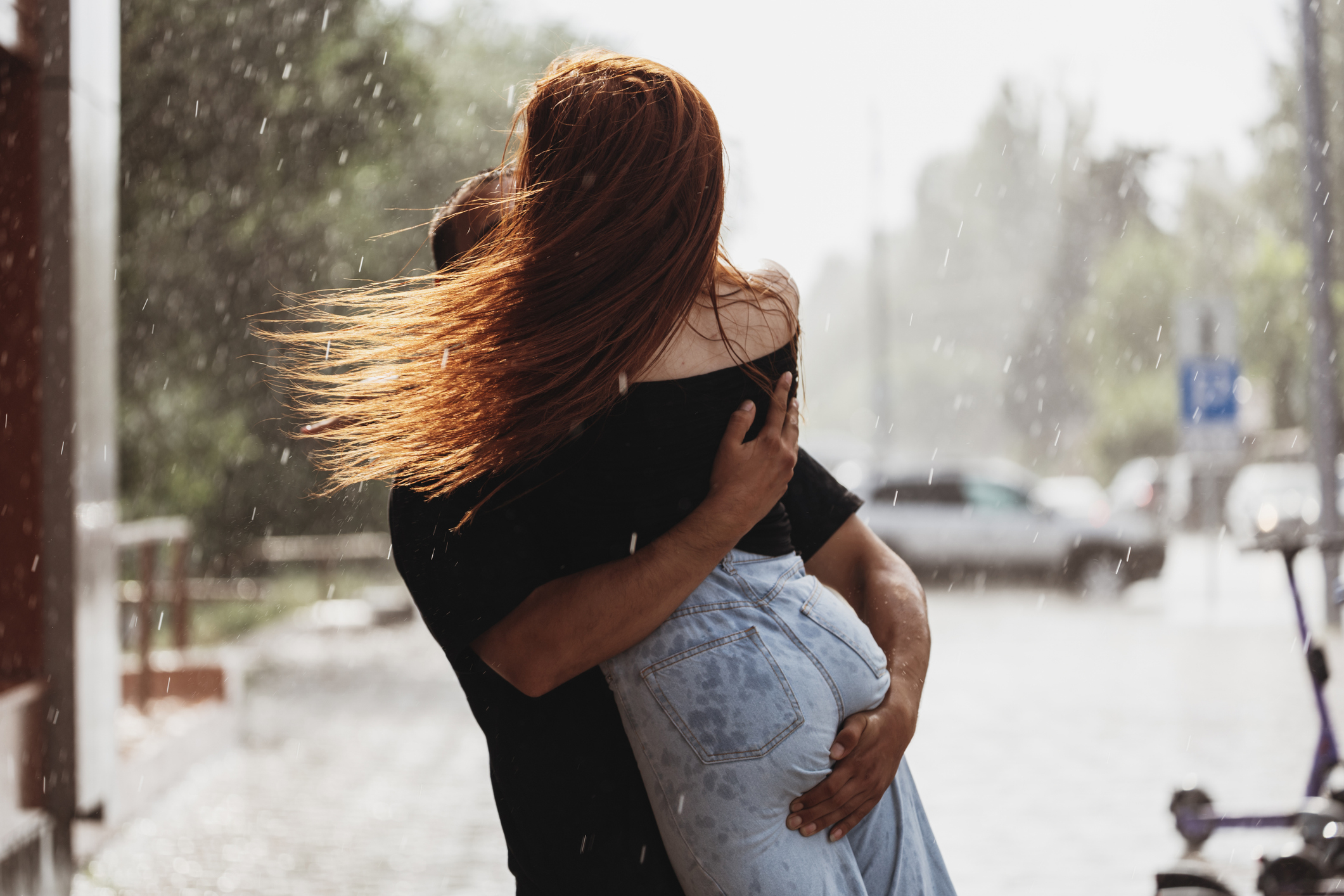 Two individuals embracing under rain, one wearing a denim skirt; faces obscured by hair