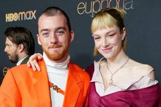 Two people smiling at a 'Euphoria' event, one in an orange suit and the other in a burgundy outfit