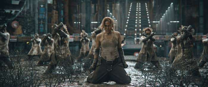 Jennifer kneeling amidst destruction with distressed clothing, in a tense dance sequence