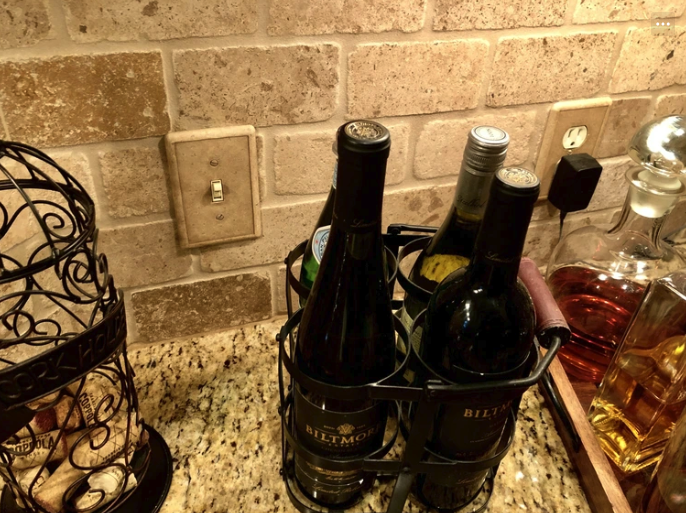 Three bottles of wine in a metal holder on a kitchen counter with a brick backsplash