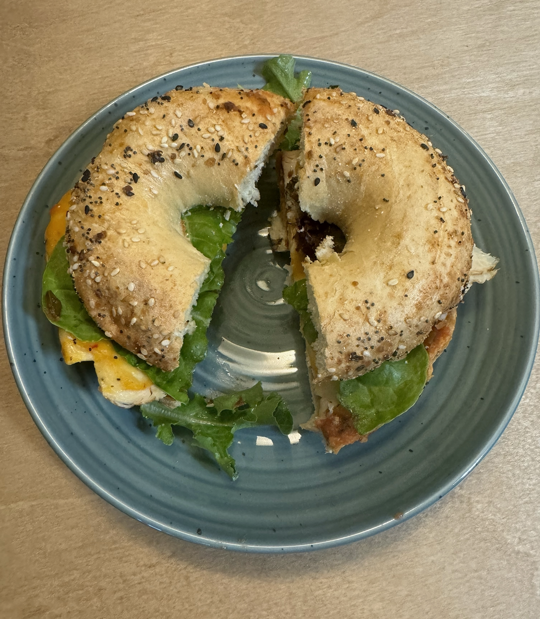 An everything bagel cut in half with chicken, cheese, and greens on a plate