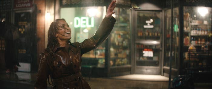 Jennifer in a coat smiling upwards as a bird flies near her hand in a nighttime urban setting in a scene from the film