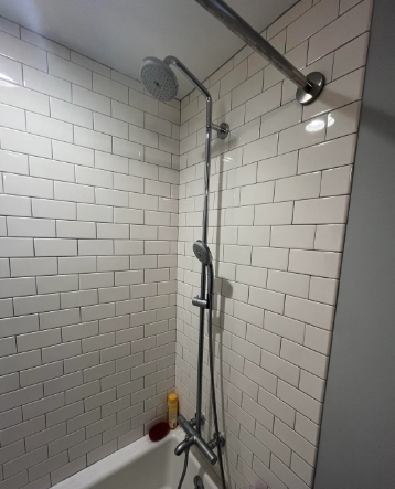 A modern shower with an adjustable height showerhead and handheld option mounted on tiled wall