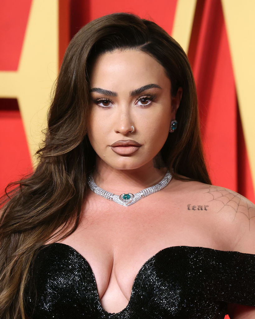 Demi Lovato wearing a black sequined outfit with a wide neckline and a diamond choker, looking at the camera
