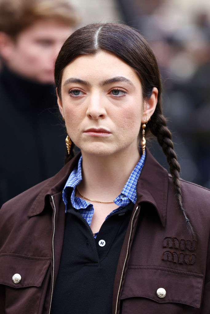 Person with braids wearing a checkered shirt under a jacket with embellished buttons