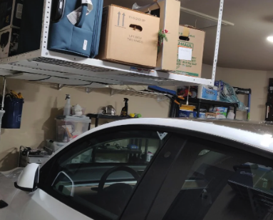 Garage interior with overhead storage shelves holding various boxes and a white car parked below