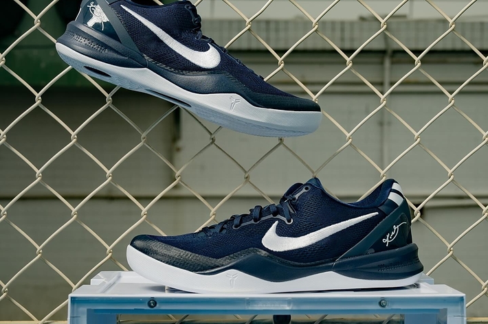 Pair of sneakers suspended on a fence above a shoebox, with a sports-court backdrop