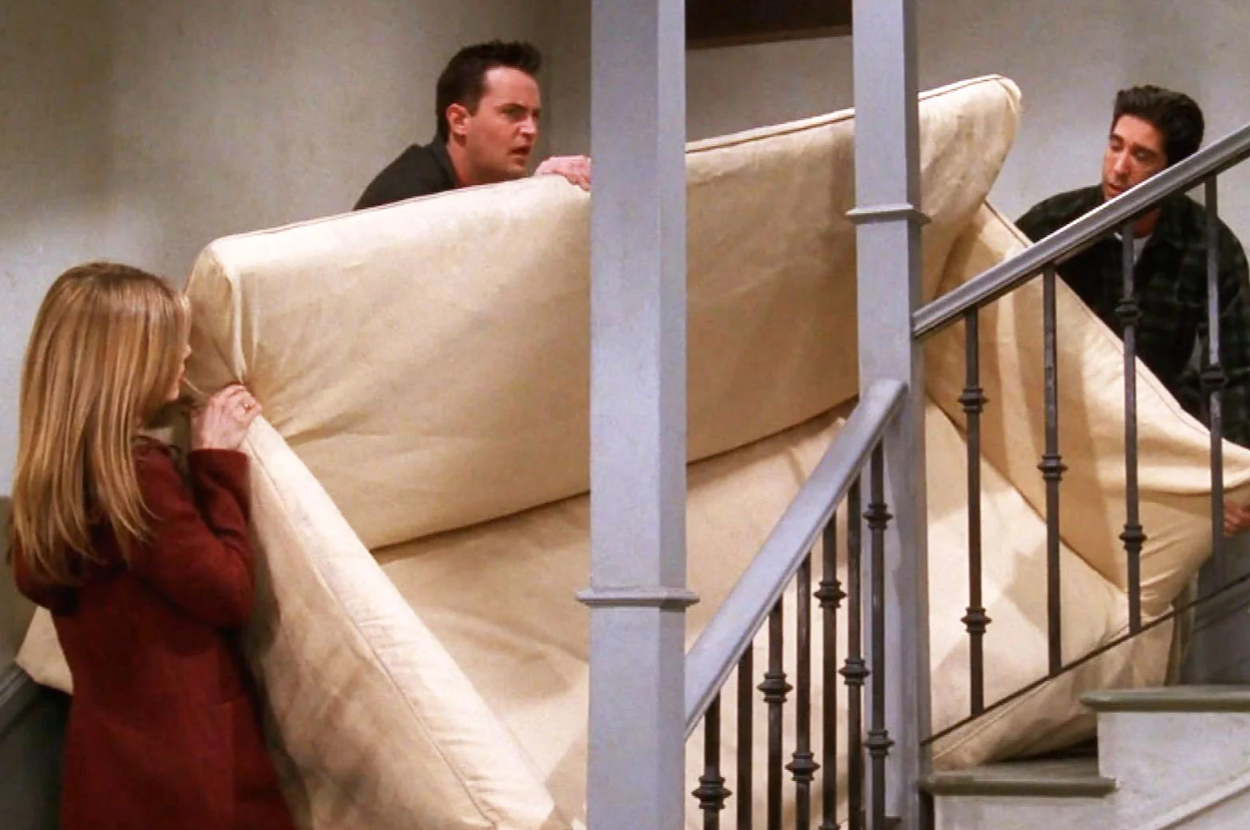 Three individuals, Rachel Green, Chandler Bing, and Joey Tribbiani from Friends, carry a couch up the staircase