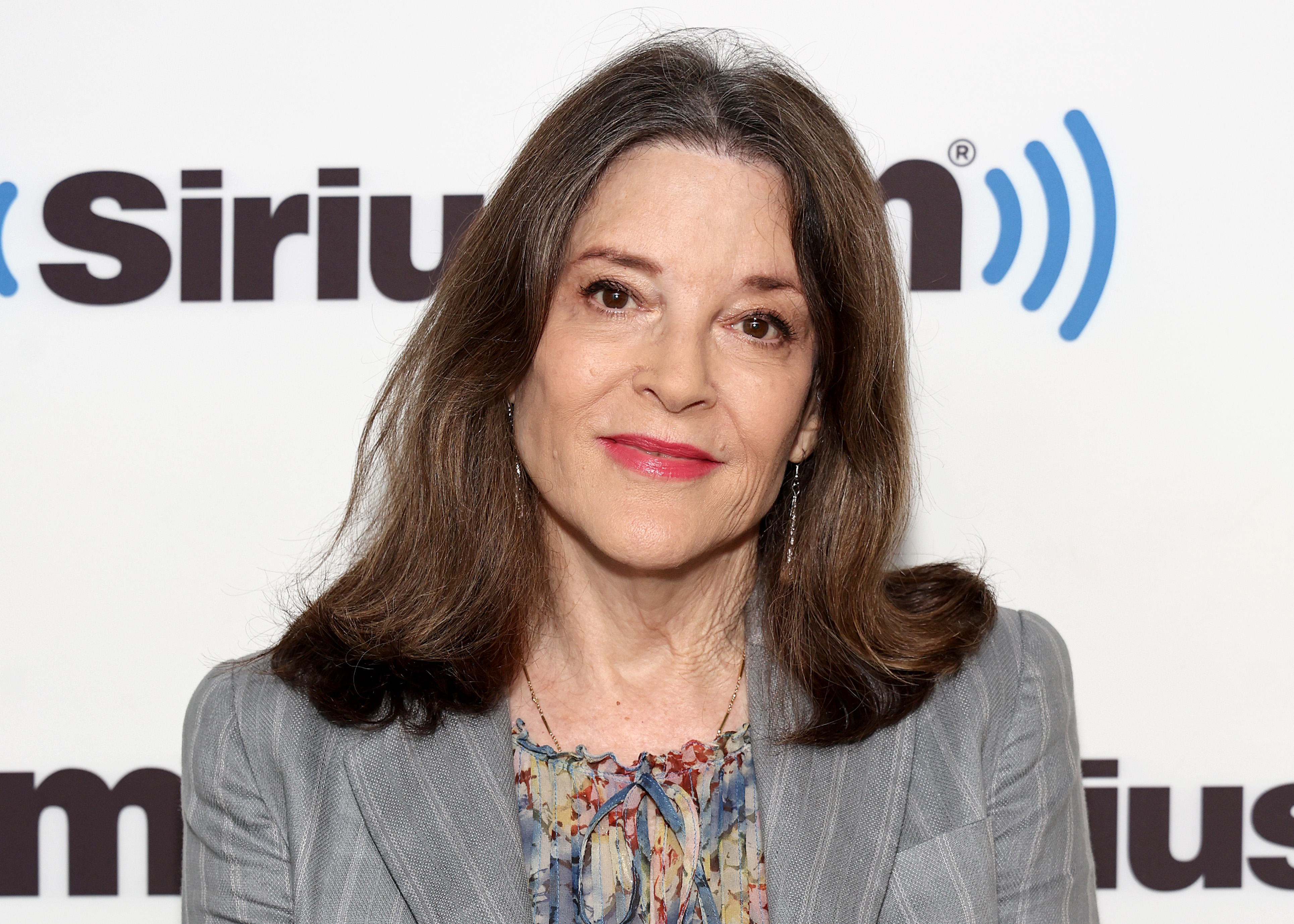 Marianne Williamson  at a SiriusXM event wearing a floral blouse and blazer