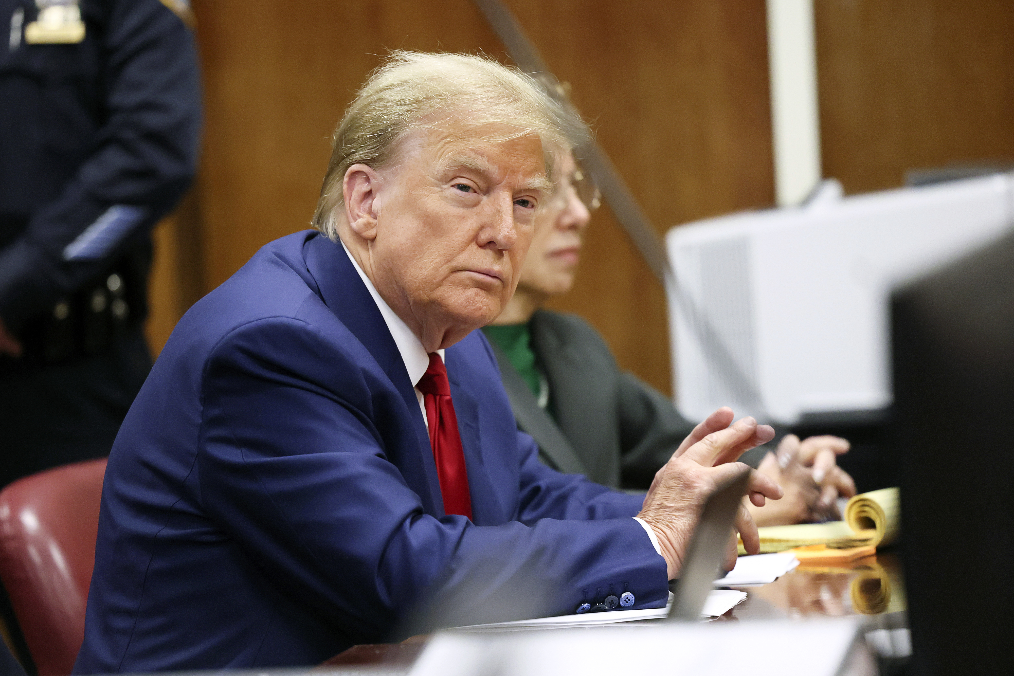 Former President Donald Trump sitting in court with documents on a table, looking towards the camera