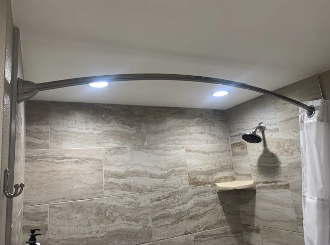 A curved shower rod with a mounted light fixture in a tiled bathroom with a showerhead and curtain