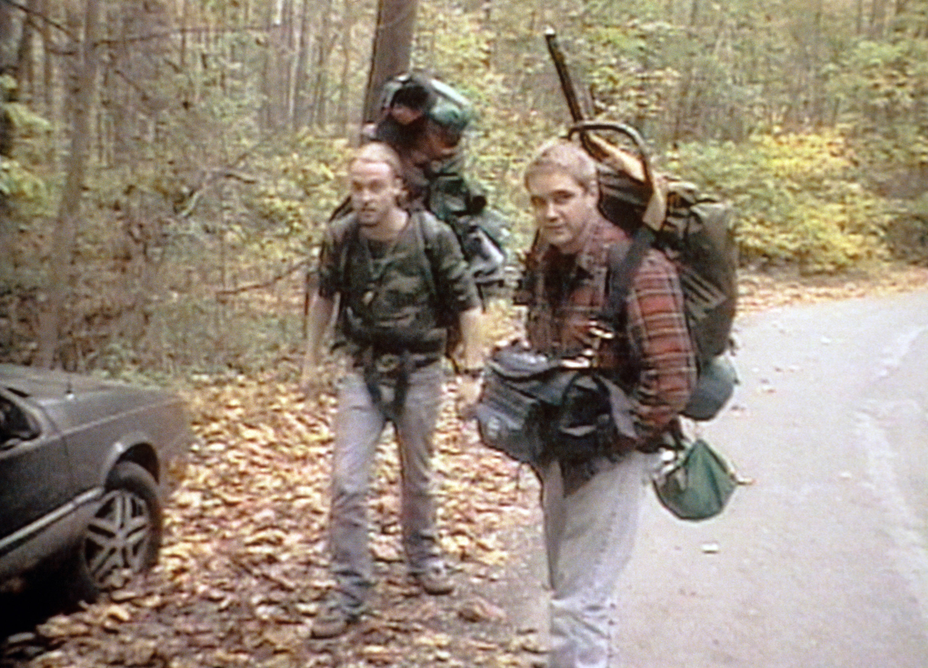 Three people with backpacks and cameras trekking on a leaf-covered road, hinting at an outdoor adventure