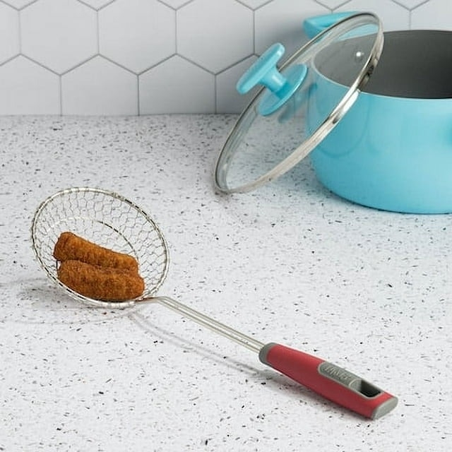 A kitchen counter with a frying pan, lid, and a mesh strainer with one chicken nugget