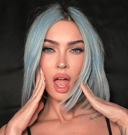 Woman with blue hair and black top poses with her hands on her face