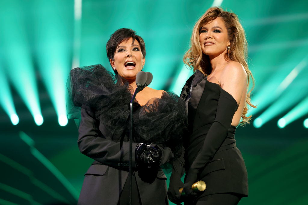 Two women on stage, one in a black dress with voluminous sleeves, the other in a strapless dress