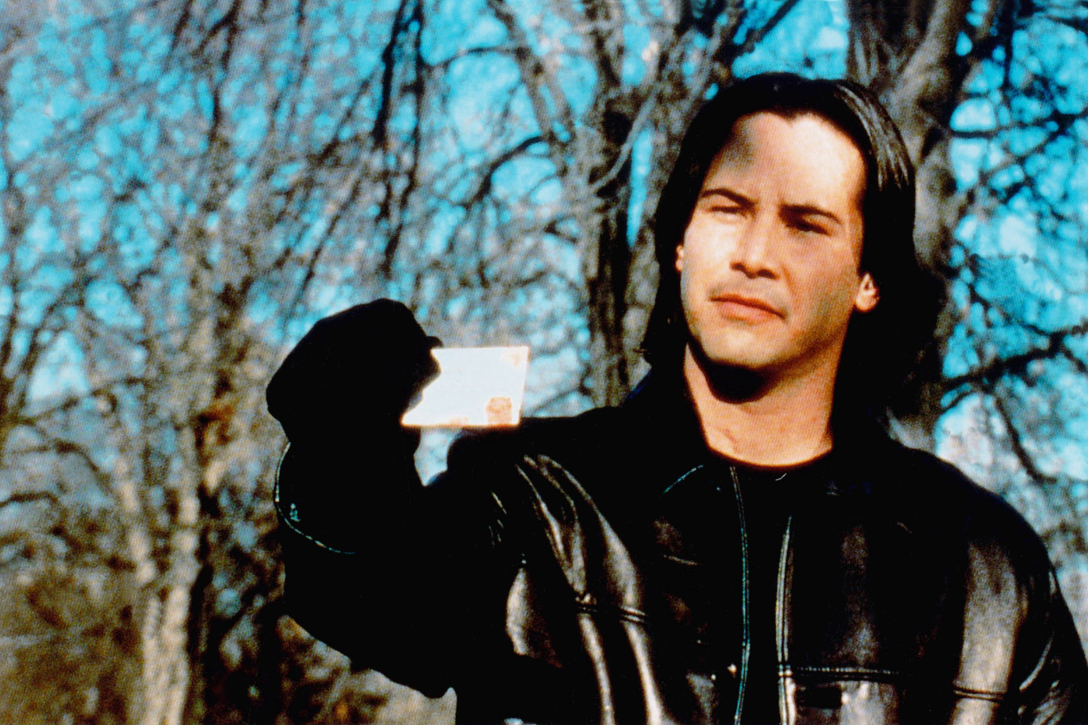 Man in leather jacket holding up a small card with a reflective surface, standing outdoors
