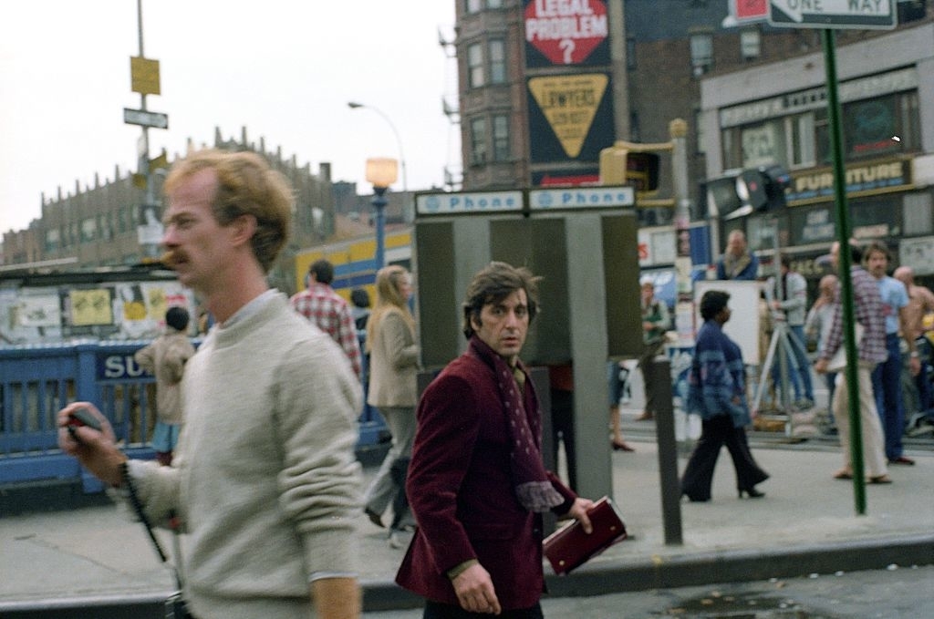Al Pacino walking on set in NYC with other pedestrians and storefronts in the background