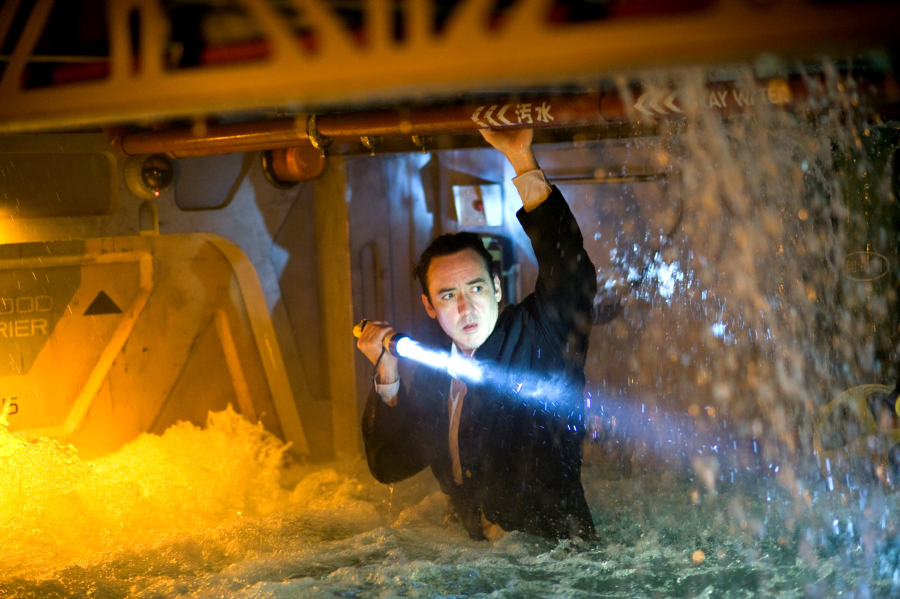 In a scene, John Cusack in a suit clings to a vehicle&#x27;s underside with a flashlight in water