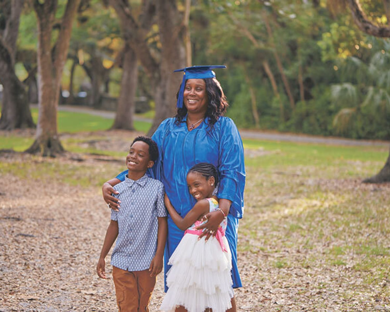 Graduate in cap and gown smiling with two children outdoors, conveying a sense of achievement and family support