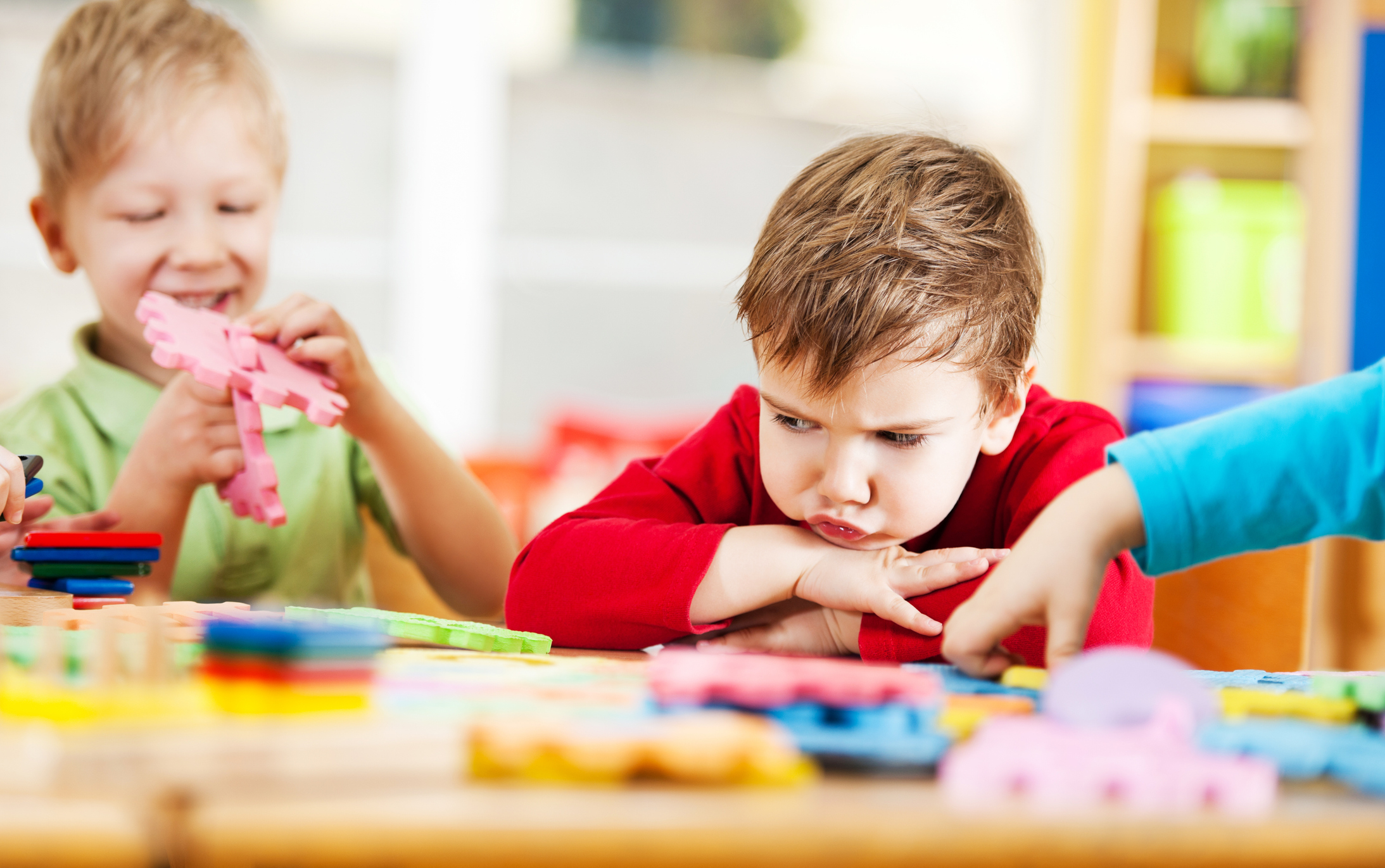 Three children engaged in play with colorful puzzle pieces at a table