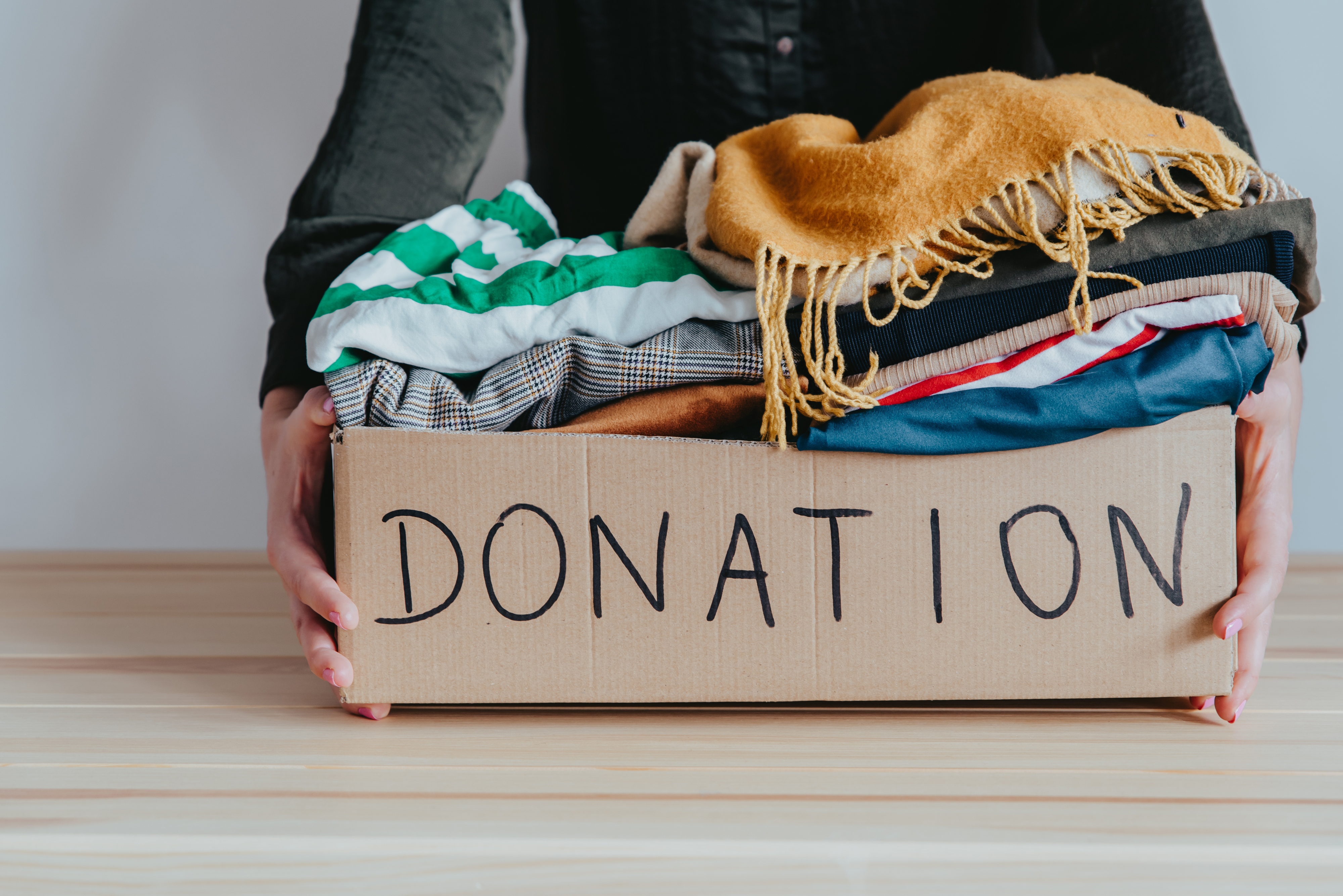 Person holding a cardboard box labeled &quot;DONATION&quot; filled with various folded clothes